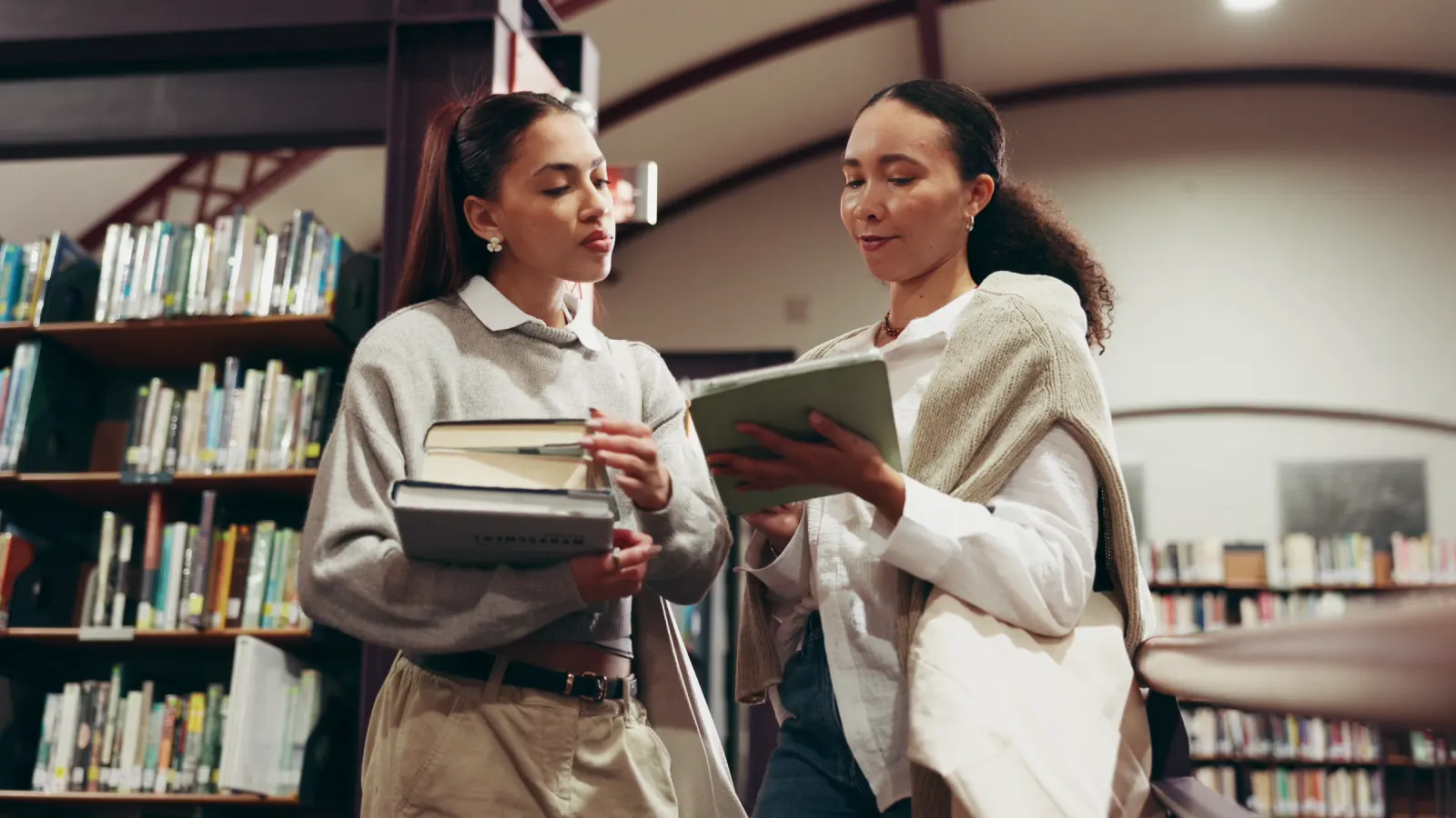 Readers among library shelves, books in hand.